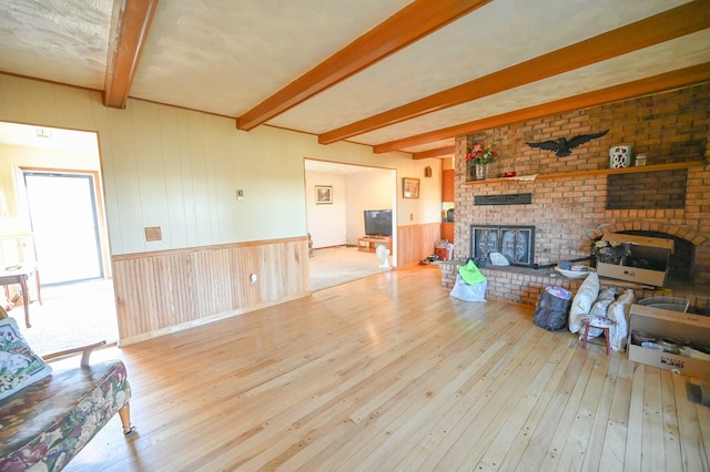 living room with a brick fireplace, light hardwood / wood-style flooring, wood walls, and beamed ceiling