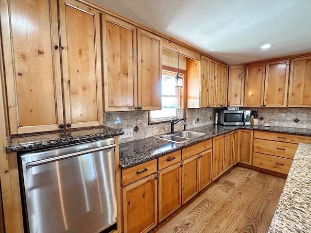 kitchen with dark stone counters, sink, tasteful backsplash, light wood-type flooring, and appliances with stainless steel finishes