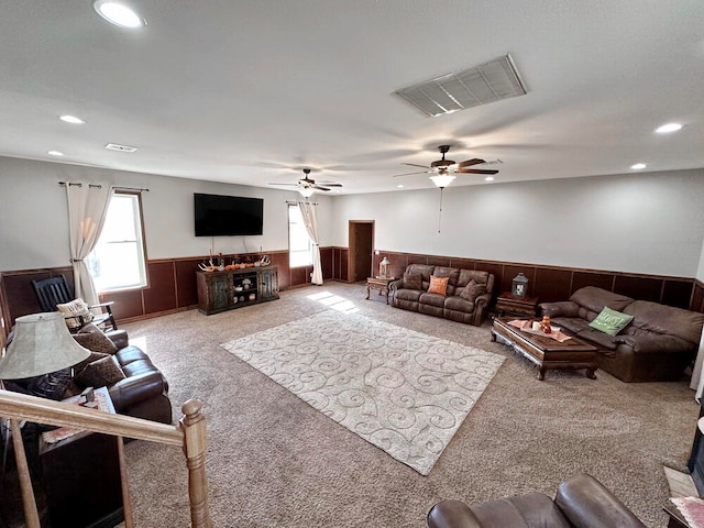 living room featuring ceiling fan, wooden walls, and light carpet