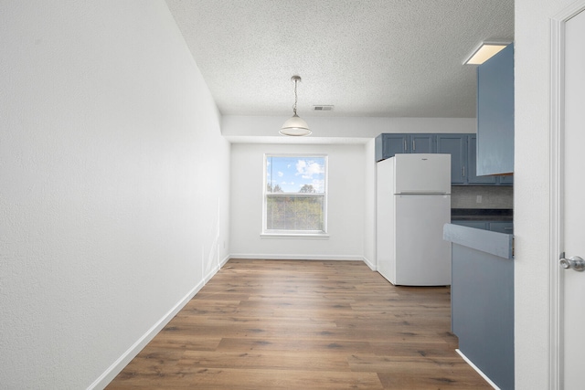 kitchen featuring dark hardwood / wood-style flooring, white refrigerator, a textured ceiling, blue cabinetry, and decorative light fixtures