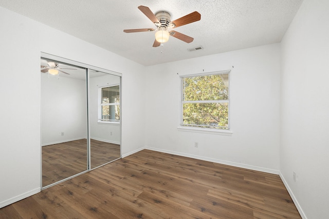 unfurnished bedroom featuring ceiling fan, a textured ceiling, a closet, and dark hardwood / wood-style flooring