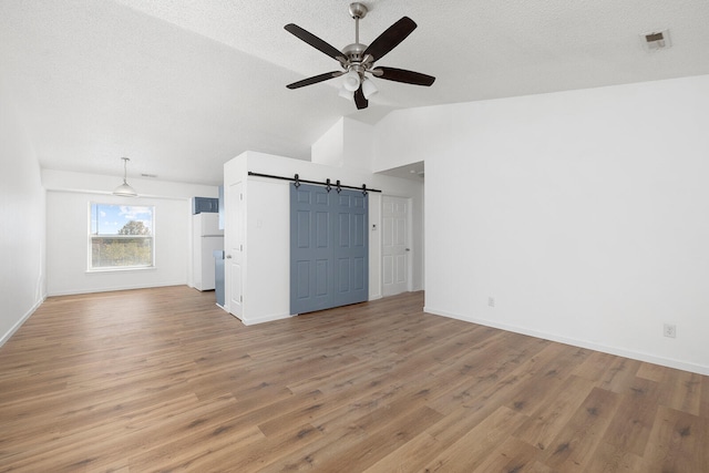 unfurnished living room with a barn door, ceiling fan, light hardwood / wood-style flooring, and lofted ceiling