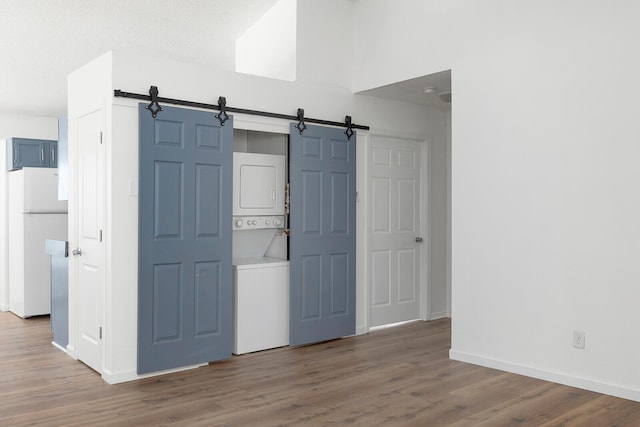 unfurnished bedroom with stacked washing maching and dryer, hardwood / wood-style flooring, a barn door, and white refrigerator