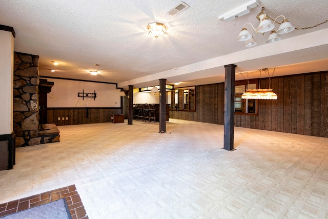 basement featuring wooden walls, a textured ceiling, and a notable chandelier