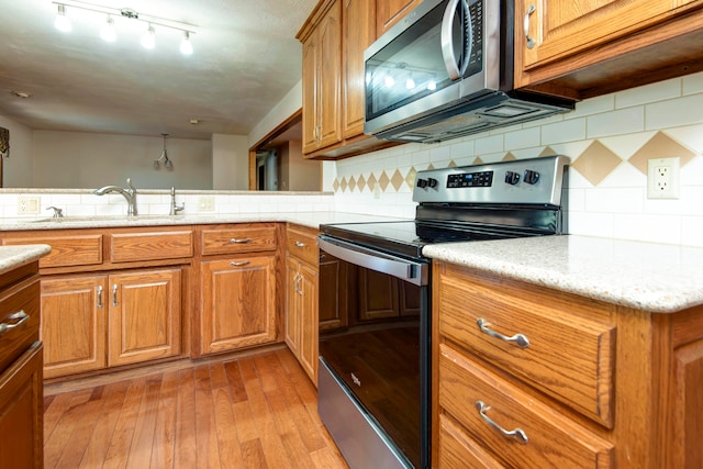 kitchen featuring stainless steel appliances, sink, tasteful backsplash, light stone countertops, and light hardwood / wood-style flooring