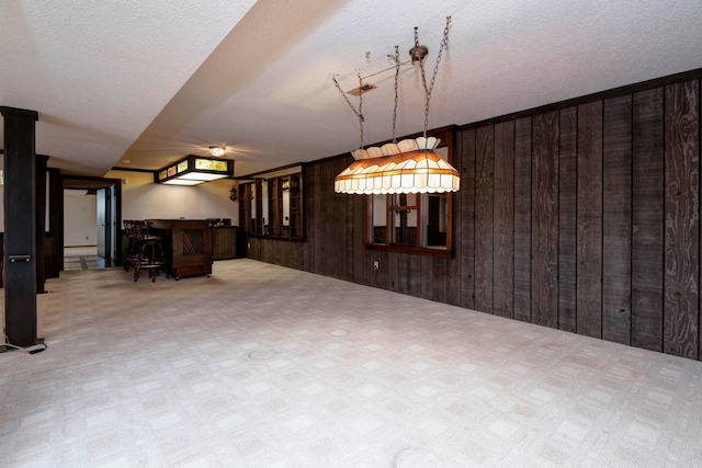 unfurnished dining area with wooden walls, a textured ceiling, and bar