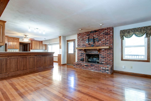 unfurnished living room with a brick fireplace, light wood-type flooring, a textured ceiling, and ceiling fan