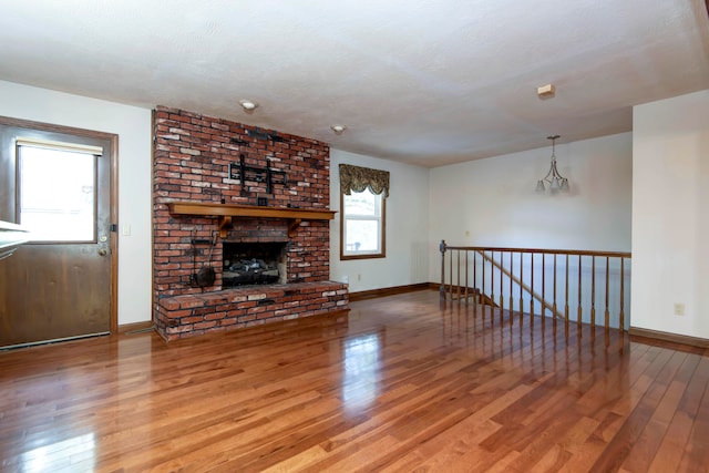 unfurnished living room featuring a brick fireplace, wood-type flooring, a textured ceiling, and a notable chandelier