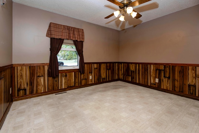 empty room featuring wooden walls, a textured ceiling, light colored carpet, and ceiling fan