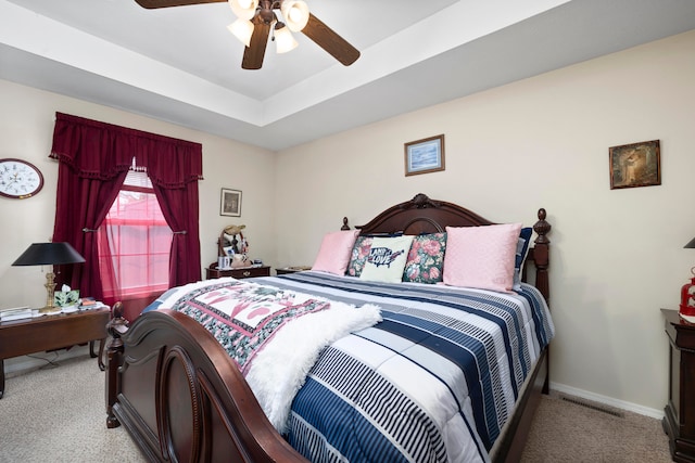 bedroom with light carpet, ceiling fan, and a raised ceiling