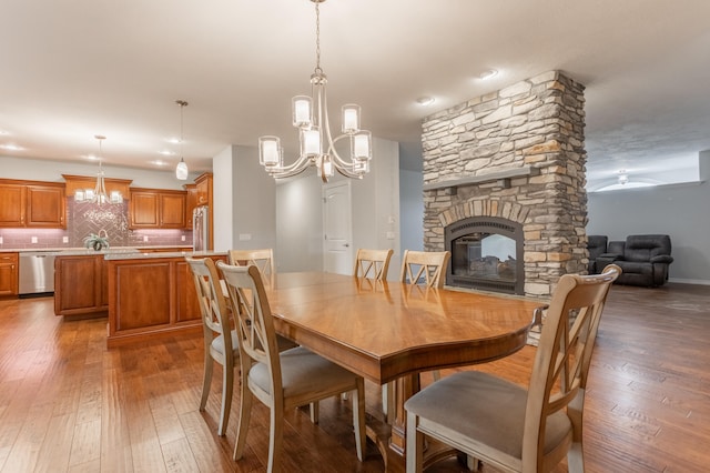 dining space featuring a stone fireplace, ceiling fan with notable chandelier, and wood-type flooring