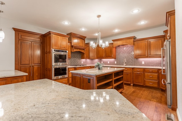 kitchen featuring hardwood / wood-style floors, hanging light fixtures, a center island, and light stone countertops