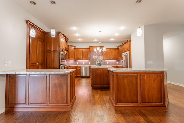 kitchen with appliances with stainless steel finishes, kitchen peninsula, tasteful backsplash, light stone countertops, and hardwood / wood-style floors
