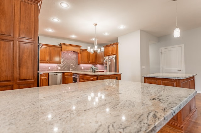 kitchen featuring stainless steel appliances, light stone countertops, decorative light fixtures, a center island, and light wood-type flooring