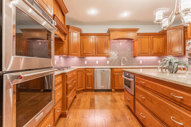 kitchen featuring light hardwood / wood-style floors, light stone counters, backsplash, appliances with stainless steel finishes, and decorative light fixtures