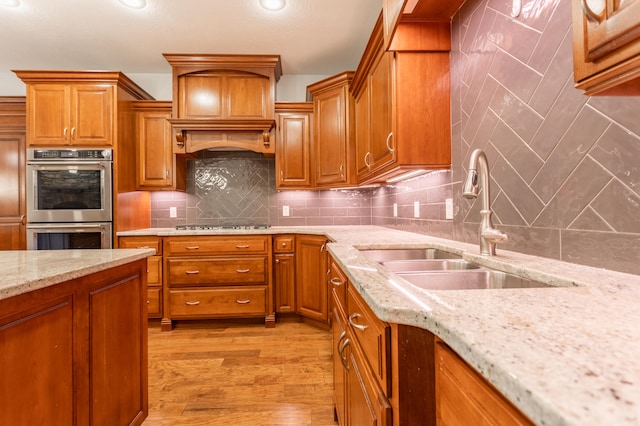 kitchen with stainless steel appliances, light stone counters, sink, tasteful backsplash, and light hardwood / wood-style flooring