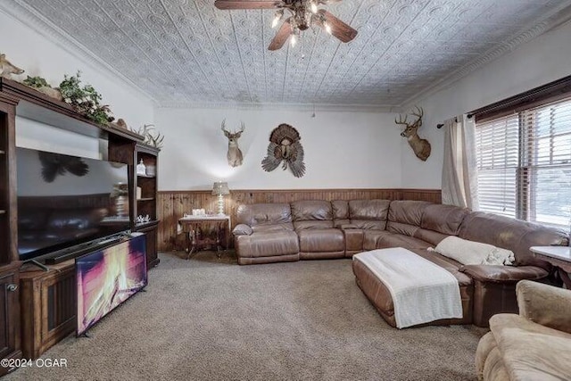 carpeted living room featuring ceiling fan, wooden walls, and crown molding