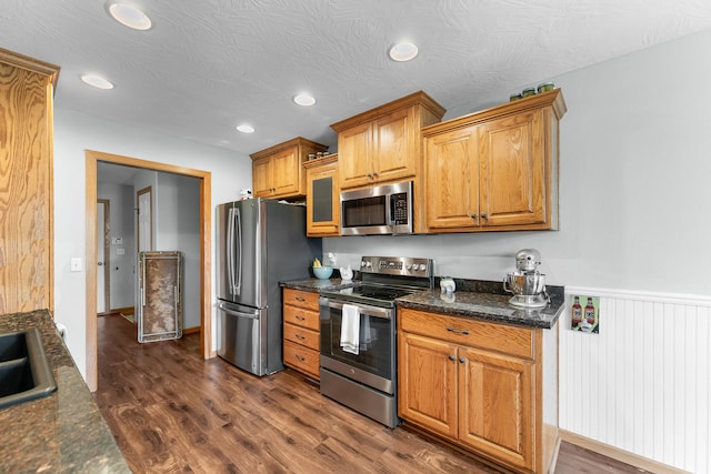 kitchen featuring sink, appliances with stainless steel finishes, dark stone counters, a textured ceiling, and dark hardwood / wood-style flooring