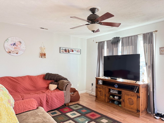 living room featuring light hardwood / wood-style floors, ceiling fan, and a textured ceiling