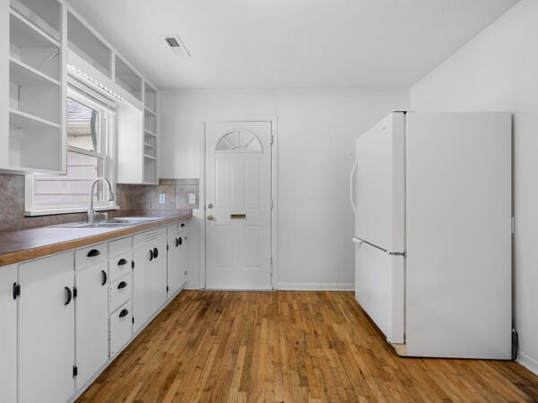 603 E Maupin St, Bolivar, MO 65613 - kitchen featuring freestanding refrigerator, a sink, open shelves, tasteful backsplash, and wood finished floors