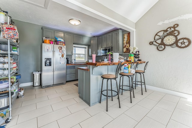 kitchen featuring butcher block counters, kitchen peninsula, appliances with stainless steel finishes, a kitchen breakfast bar, and lofted ceiling