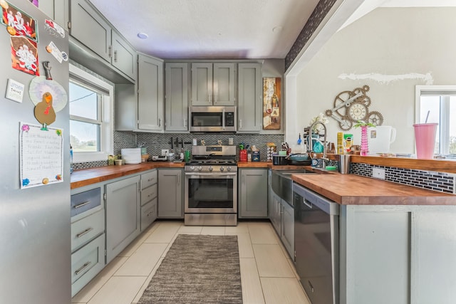 kitchen with butcher block counters, gray cabinets, stainless steel appliances, and tasteful backsplash