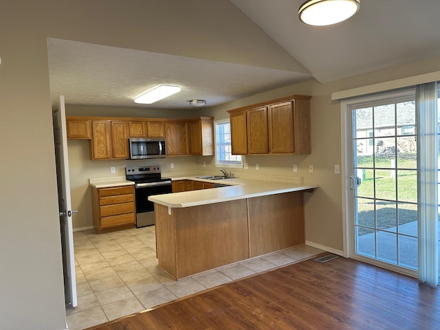 kitchen with stainless steel appliances, a healthy amount of sunlight, light wood-type flooring, and kitchen peninsula