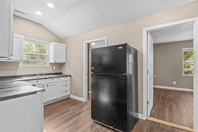 kitchen featuring dark hardwood / wood-style flooring, black refrigerator, white cabinetry, and vaulted ceiling