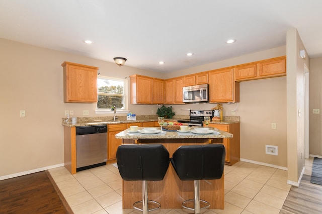 kitchen with stainless steel appliances, a breakfast bar, light stone counters, light tile patterned floors, and a center island