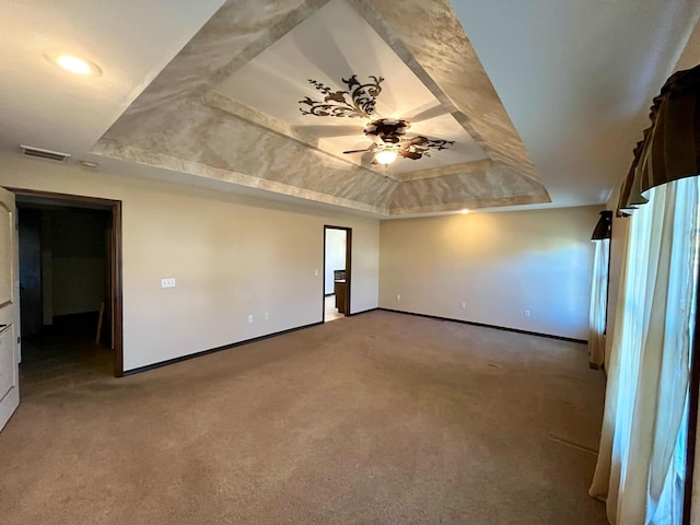 empty room with a raised ceiling, ceiling fan, and carpet floors