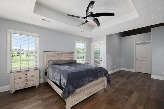 bedroom with dark wood-type flooring, ceiling fan, and a tray ceiling