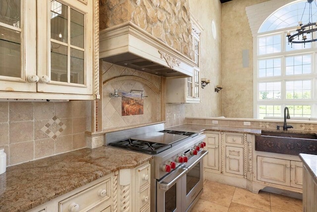 kitchen featuring double oven range, cream cabinetry, sink, and backsplash