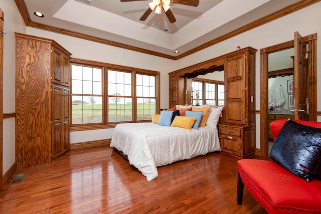 bedroom featuring multiple windows, hardwood / wood-style floors, ceiling fan, and a raised ceiling