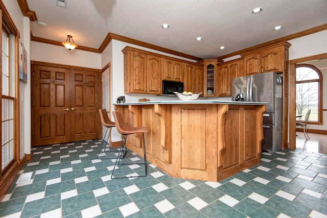 kitchen with crown molding, a textured ceiling, stainless steel fridge with ice dispenser, a kitchen bar, and kitchen peninsula