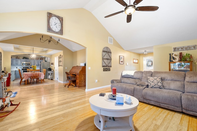 living room with ceiling fan with notable chandelier, light hardwood / wood-style flooring, and vaulted ceiling