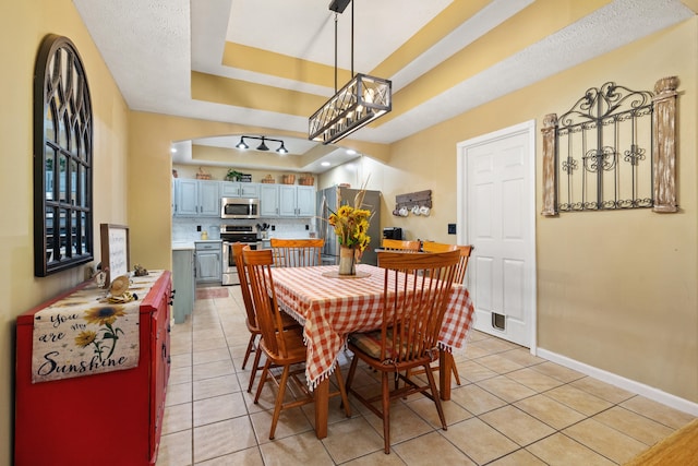 tiled dining space with a textured ceiling, a notable chandelier, and a raised ceiling