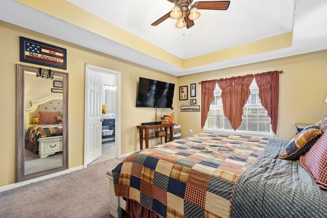 bedroom with connected bathroom, a tray ceiling, carpet flooring, and ceiling fan