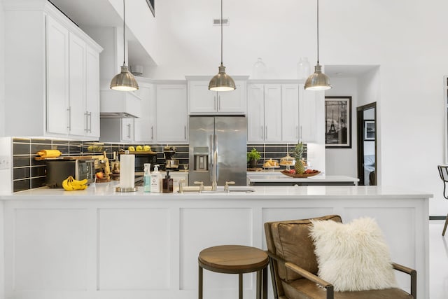 kitchen featuring white cabinetry, decorative backsplash, hanging light fixtures, stainless steel refrigerator with ice dispenser, and a breakfast bar