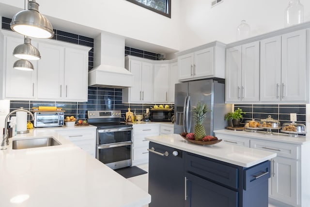 kitchen featuring white cabinets, stainless steel appliances, decorative light fixtures, and premium range hood