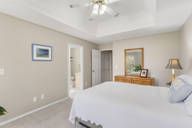 carpeted bedroom featuring a closet, a tray ceiling, ceiling fan, and ensuite bathroom