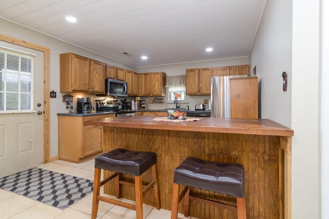 kitchen with a kitchen bar, wooden counters, kitchen peninsula, light tile patterned flooring, and appliances with stainless steel finishes