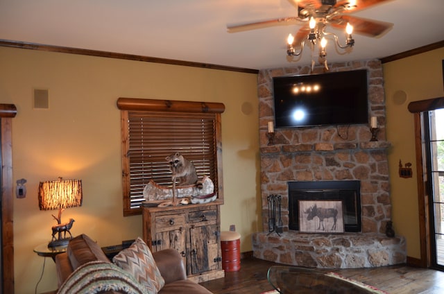 living room with ceiling fan, wood-type flooring, a stone fireplace, and crown molding