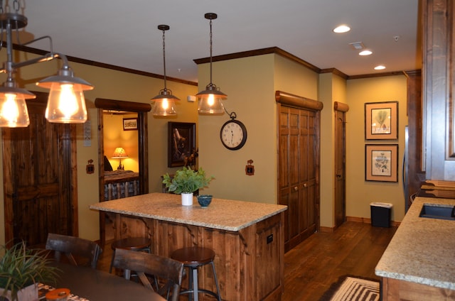 kitchen featuring ornamental molding, dark hardwood / wood-style floors, hanging light fixtures, a kitchen breakfast bar, and a center island