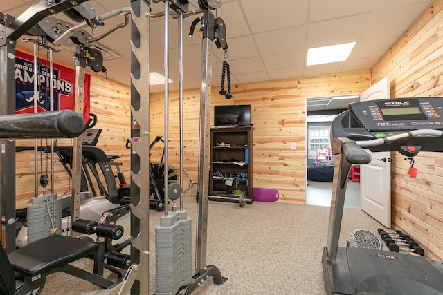 exercise room featuring wood walls, a paneled ceiling, and carpet floors