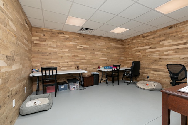 office area with wood walls, concrete flooring, and a drop ceiling