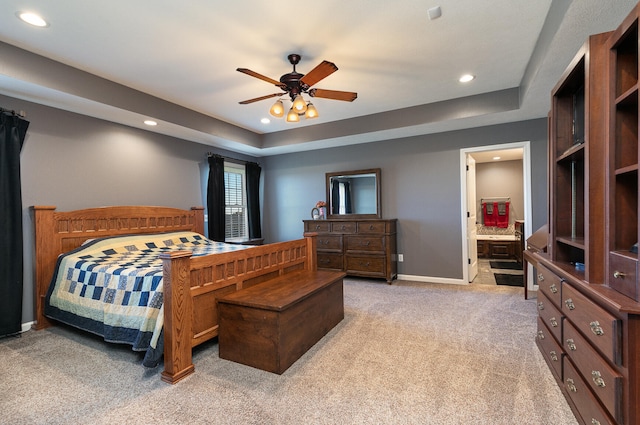 bedroom featuring ceiling fan, ensuite bath, a tray ceiling, and light colored carpet