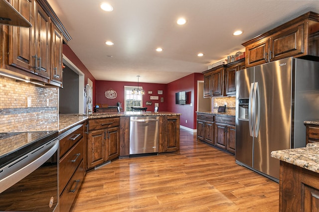 kitchen with hardwood / wood-style floors, backsplash, stone countertops, appliances with stainless steel finishes, and decorative light fixtures