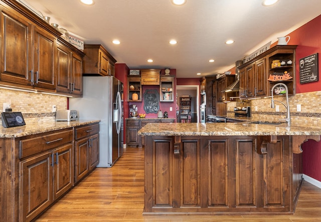 kitchen with appliances with stainless steel finishes, light hardwood / wood-style floors, backsplash, and light stone countertops