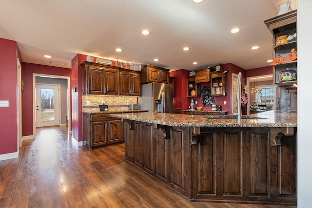 kitchen featuring dark hardwood / wood-style floors, light stone countertops, stainless steel refrigerator with ice dispenser, a breakfast bar, and kitchen peninsula