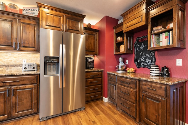 kitchen featuring stone countertops, light hardwood / wood-style flooring, backsplash, and stainless steel fridge